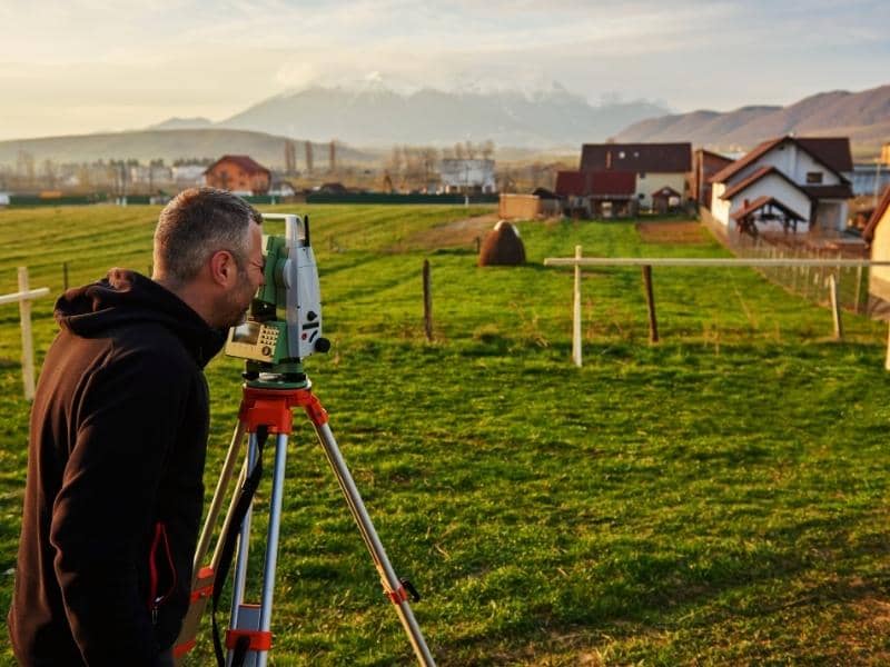Residential land survey showing a surveyor using equipment to measure property boundaries in an open field